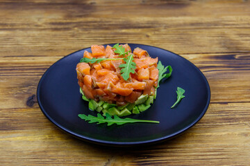 Salmon tartare with avocado and arugula on wooden table