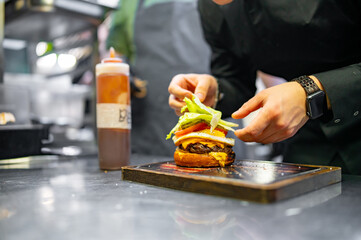 chef hand cooking cheeseburger with vegetables and egg on restaurant kitchen