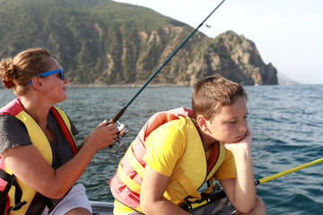 Mother with son fishing with rod in sea