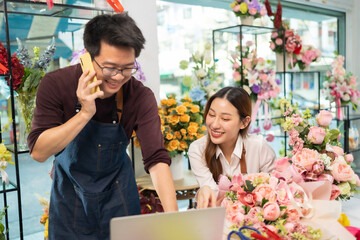 Asian man florist talking on smartphone using laptop at florist.portrait of mature male small business owner using laptop and looking at camera in flower shop