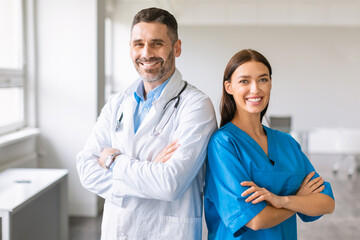 Confident caucasian colleagues male doctor and female nurse, wearing coats, posing with folded...