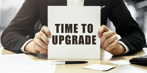 Businessman holding a white card with text TIME TO UPGRADE on office background