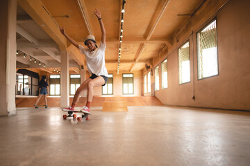 Unidentified young woman in casual sports clothing learning and practicing skateboarding while trying to balance with arms extended on artificial indoor small slide in skating studio during daytime