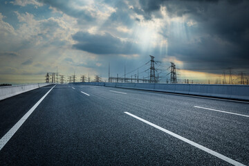 Asphalt road and high voltage power tower with sky ray background