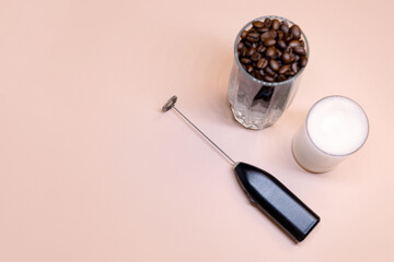 Milk foam maker with glass of milk on pink peach background.