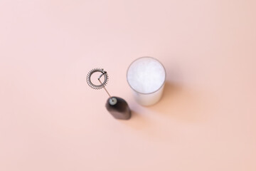 Milk foam maker with glass of milk on pink peach background.