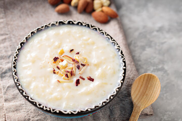 Indian rice kheer with nuts on a gray background. Bowl with rice pudding and a linen napkin on concrete. Top view