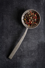Big old spoon with peppercorn on black background