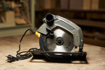 circular saw with electric cable stands on a wooden table in a workshop
