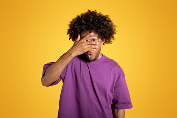 Fototapeta na wymiar Sad shocked adult african american curly guy in purple t-shirt covers face with hands