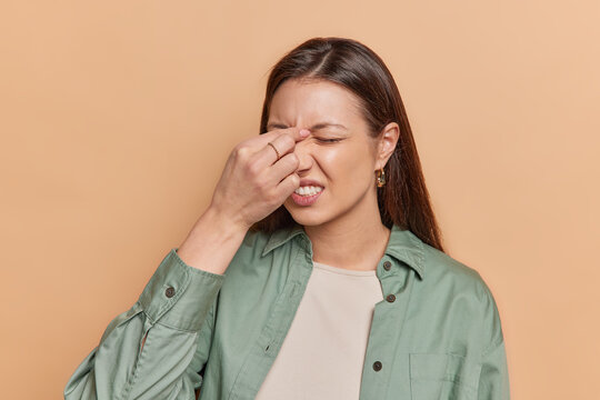 Tired Brunette Woman Touching Nose Between Closed Eyes Suffers From Eye Tension After Working On Computer Tries To Relieve Pain Suffers From Headache Wears Green Shirt Isolated Over Brown Background