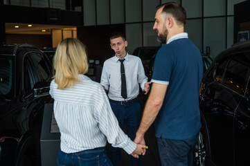 Obraz premium Happy caucasian couple choosing a new car in a car dealership. 