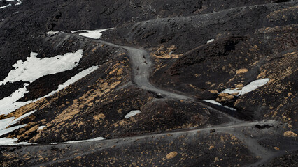 Snow melts on Etna volcano in spring. Panorama of uneven ground full of lava earth and craters....