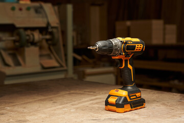 a beautiful black and yellow electric screwdriver with sharp corners with a replaceable battery stands on a wooden workbench in a carpentry trowel