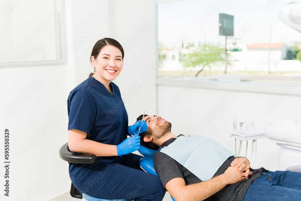 Wall mural Smiling woman dentist treating a latin male patient