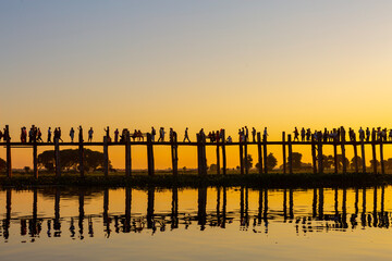 Unidentified people walk on U Bein bridge at sunset in Myanmar. U Bein bridge is the longest teak bridge in the world, Amarapura, Myanmar