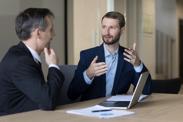 Ambitious young business man talking to boss, elder colleague at workplace, presenting project plan, strategy, reporting work result. Employer interviewing job candidate
