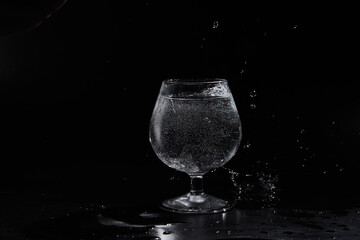 Pouring purified fresh water in glass on mirror background. Glass cup with water and bubbles on a black background