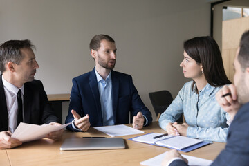 Serious successful young boss, CEO, executive talking to team on corporate brainstorming meeting, instructing employees. Business partners discussing startup project buying