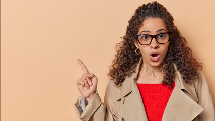 Surprised Brazilian woman cannot believe own eyes points finger at upper left corner gasps from...