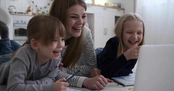 Slow motion shot of caucasian mother and daughters laughing while watching movie over laptop and relaxing on floor at home