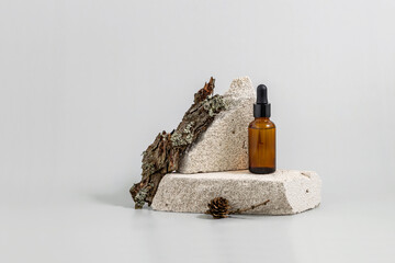  bottle with an essential oil pipette on a podium made of stone and lichens on a gray background