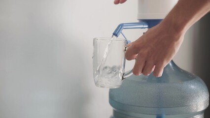 Pour fresh clean water from a large blue gallon into a glass. Clean drinking bottled water from the...