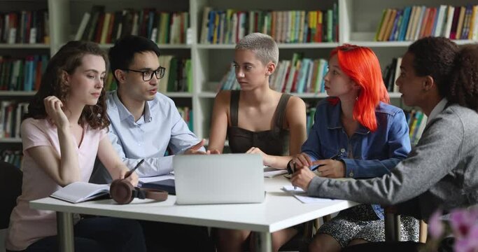 Group of five college students talking gathered together in library, share opinions, ideas, think on joint project, make assignment, brainstorm, engaged in teamwork. Education, meeting of groupmates
