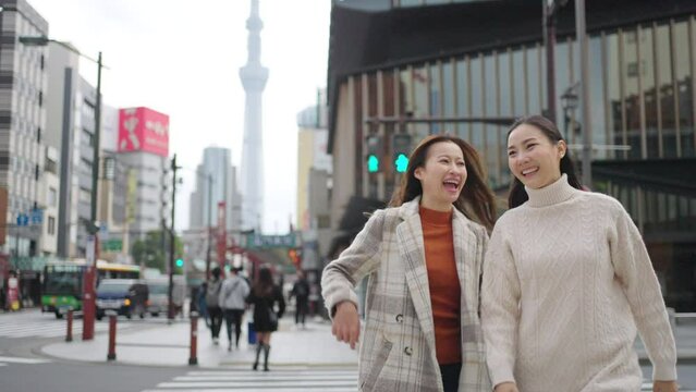 Asian woman friends crossing street crosswalk with crowd of people during travel together at Asakusa, Tokyo, Japan in autumn. Attractive girl enjoy urban outdoor lifestyle travel on holiday vacation.