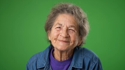 Closeup funny portrait of happy smiling toothless elderly senior old woman with wrinkled skin and grey hair on green screen background.
