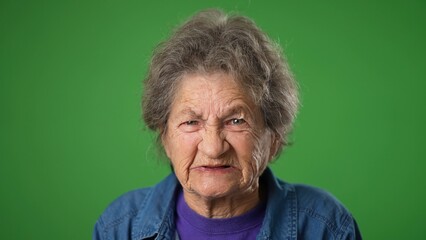 Portrait of toothless, angry upset frustrated elderly senior old woman with wrinkled skin and grey hair on green screen background. - obrazy, fototapety, plakaty