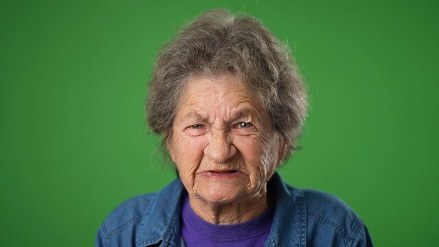 Portrait of toothless, angry upset frustrated elderly senior old woman with wrinkled skin and grey hair on green screen background.