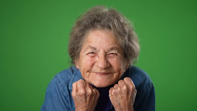Closeup funny toothless portrait of elderly senior old woman with wrinkled skin and grey hair has great success winner isolated green screen background in studio. People emotions concept