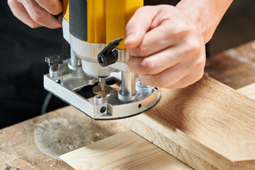 The hands of a Caucasian worker set up a position to start processing a wooden workpiece using an electric router