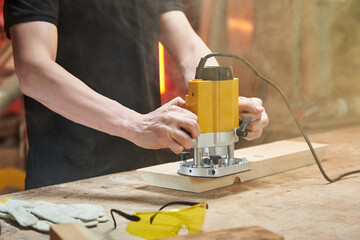 caucasian worker's hands milling the end of a wooden workpiece with an electric milling cutter and...