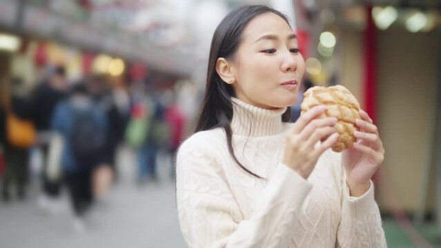 4K Happy Asian woman eating Japanese sweet bread during travel at Sensoji Temple in Asakusa, Tokyo, Japan. Attractive girl enjoy and fun urban outdoor lifestyle travel city street on holiday vacation.