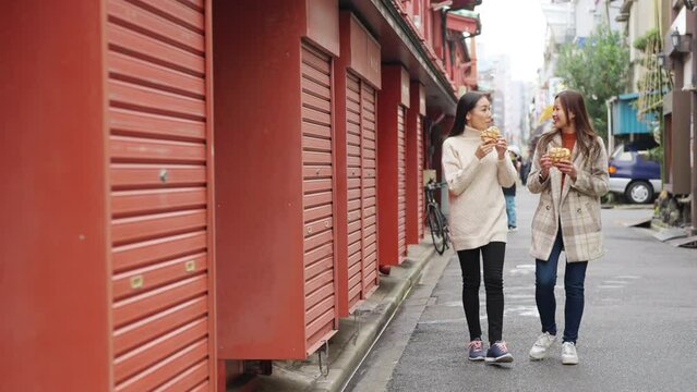 4K Happy Asian woman friends eating Japanese sweet bread together during travel at Asakusa, Tokyo, Japan. Attractive girl enjoy and fun urban outdoor lifestyle travel city street on holiday vacation.