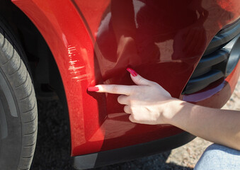 Scratches on the front bumper of a red car. A young girl driver got into a traffic accident and turns to a repair service.