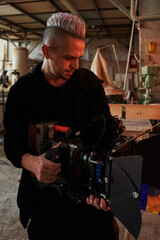 caucasian videographer with a haircut shoots on a professional movie camera holding it in his hands © Elena