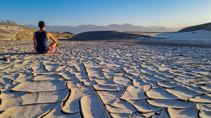 Man sitting on dry cracked clay crust at Mesquite Flat Sand Dunes in Death Valley National Park,...