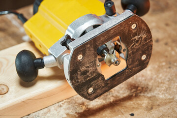 A hand router with a yellow light decorative cutter and a wooden piece lie on a table top