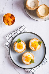 Appetizing tartlet with whipped cream, canned fruit and mint on a plate top and vertical view
