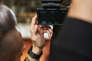 Caucasian videographer adjusts the screen of a professional movie camera on the set