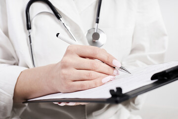 A doctor in a medical gown and with a phonendoscope fills out the form of a new adult patient on a...