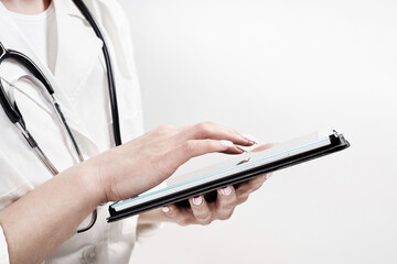 A doctor in a medical gown and with a phonendoscope fills out the form of a new adult patient on a tablet