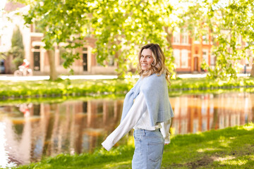 Portrait of beautiful woman smiling and turn around in park at sunny day. Outdoor portrait of a smiling curly blonde girl. Happy cheerful girl laughing at park wear sweater, white longsleeves, shorts