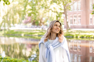 Portrait of beautiful woman smiling and look at side in park at sunny day. Outdoor portrait of a smiling curly blonde girl. Happy cheerful girl laughing at park wear sweater, white longsleeve, short. 