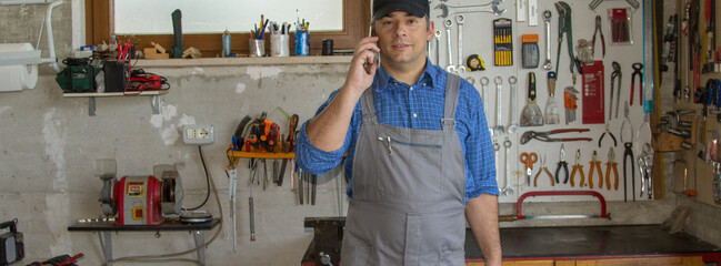Image of a handyman in his workshop talking on the phone and holding a toolbox. Answering a call for work. Horizontal banner 
