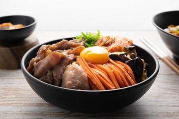 Kimchi fried rice with fried brisket and wakame seaweed and raw egg in black bowl on wooden table,(bibimbap).