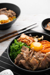 Kimchi fried rice with fried brisket and wakame seaweed and raw egg in black bowl on wooden table,(bibimbap).
